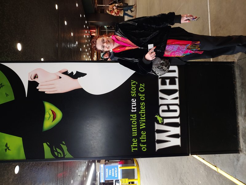Lynne at the Wicked theater, holding her tickets, beaming